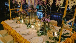 Ein festlich gedeckter Tisch mit weißen Tellern, Besteck und Gläsern, umgeben von gelben Vorhängen und floralen Tischdekorationen.