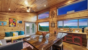 A wooden cabin interior with a bar area, large windows, and a view of the mountains.