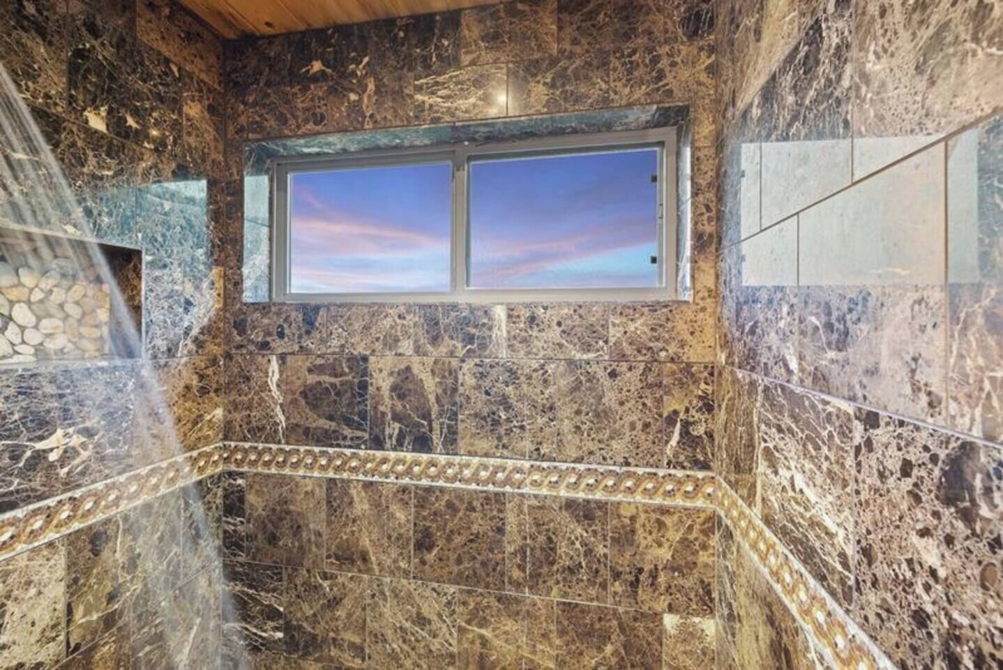 Un baño con un ventanal grande, paredes de mármol y una pared decorativa de piedra.