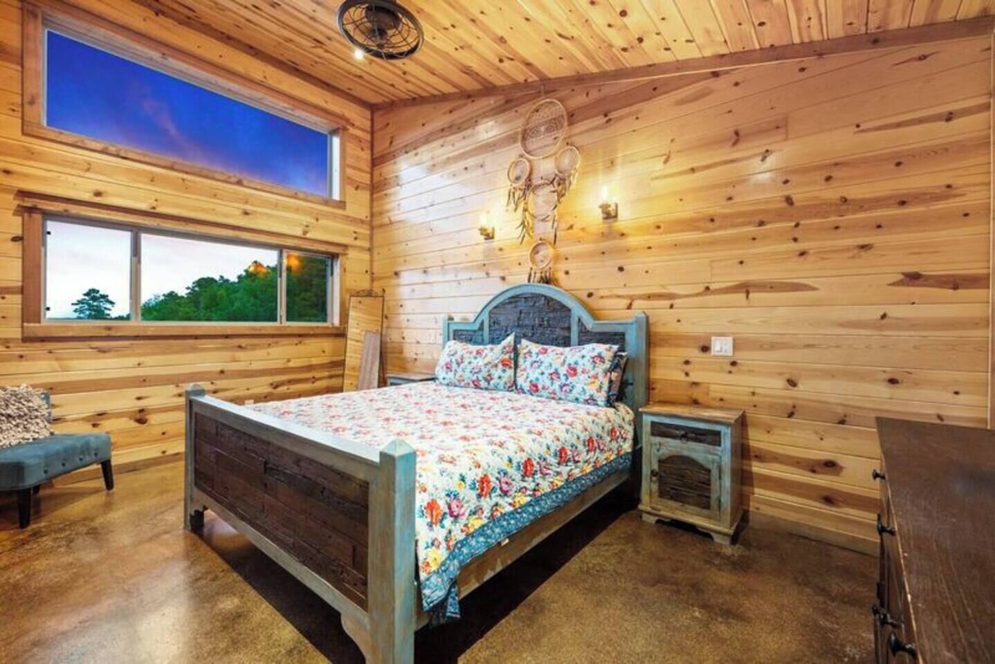 Quarto de cabana de madeira com cama, mesas de cabeceira, uma janela e vista para o exterior.