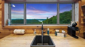 A kitchen with a large window offering a scenic view of a lake and forest.