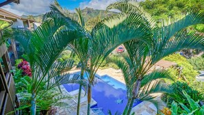 Una piscina circondata da piante tropicali, con vista su una montagna e un edificio sullo sfondo.