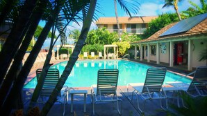 A swimming pool with lounge chairs, surrounded by palm trees and a building with a Coca-Cola sign.