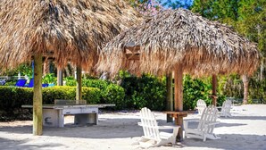 A beach area with thatched umbrellas, white chairs, and a bench.