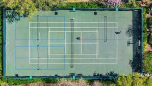 An aerial view of a tennis court with multiple courts, surrounded by greenery.