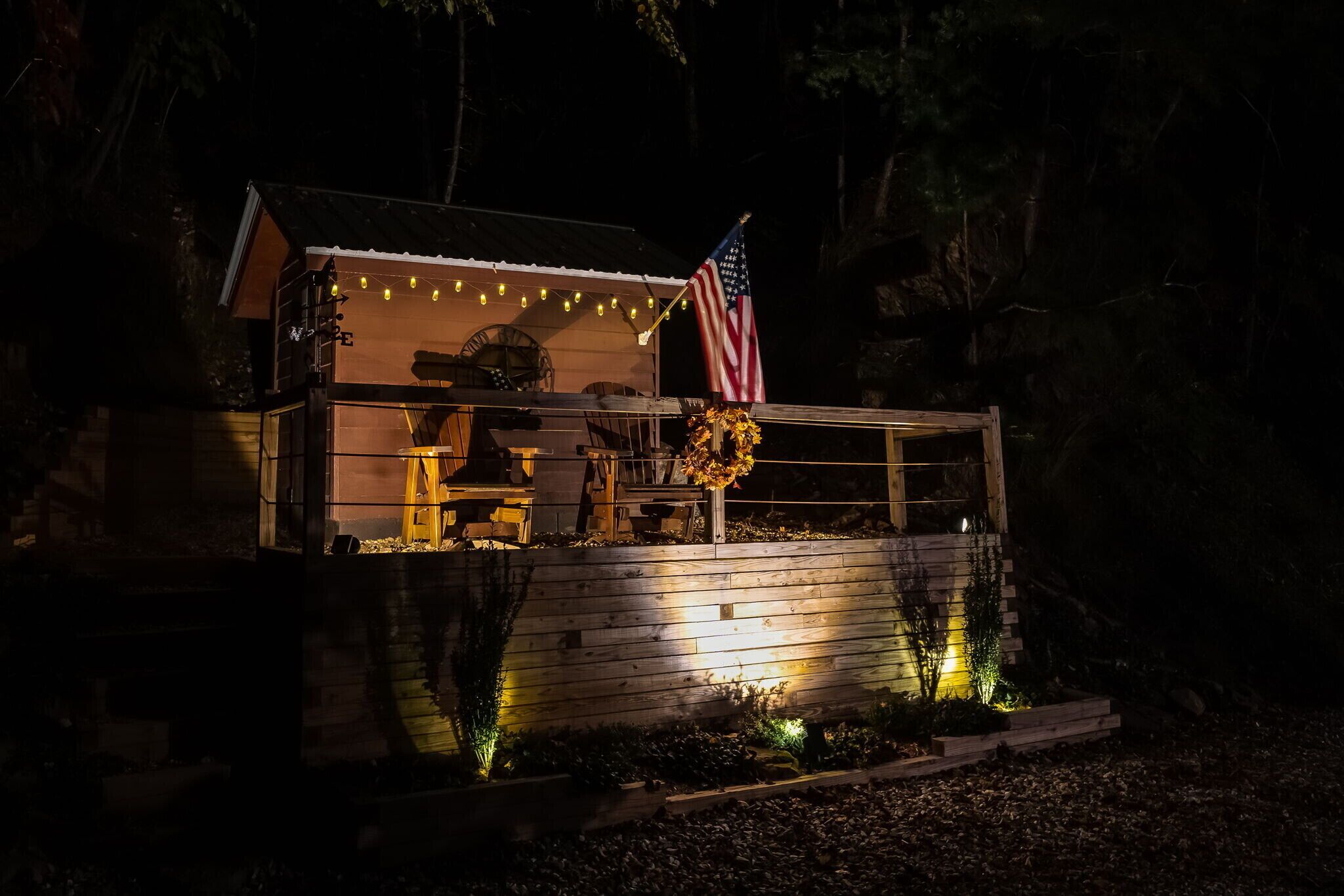 A small cabin with a porch, an American flag, and string lights.