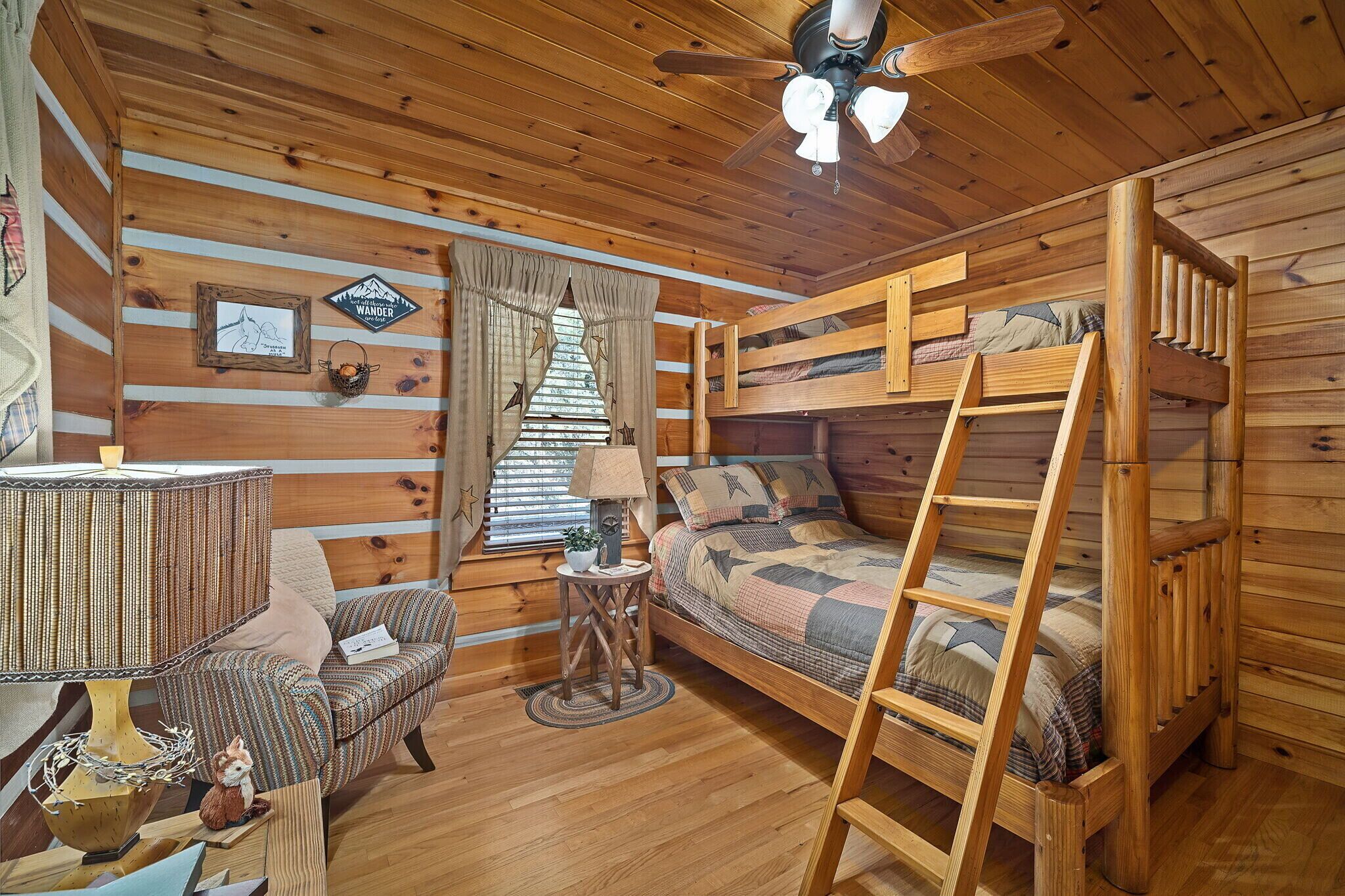 Une chambre confortable dans un chalet, avec un lit superposé, un bureau avec une lampe, une chaise et une petite table agrémentée d'une lampe et d'un objet décoratif.