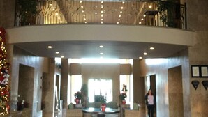 A spacious lobby with a high ceiling, a central seating area, and a balcony with railings.