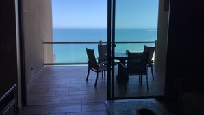 A balcony with a table and chairs, overlooking a clear view of the ocean.