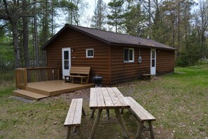 Une cabane en bois dotée d’une terrasse, de tables de pique-nique et d’un barbecue.