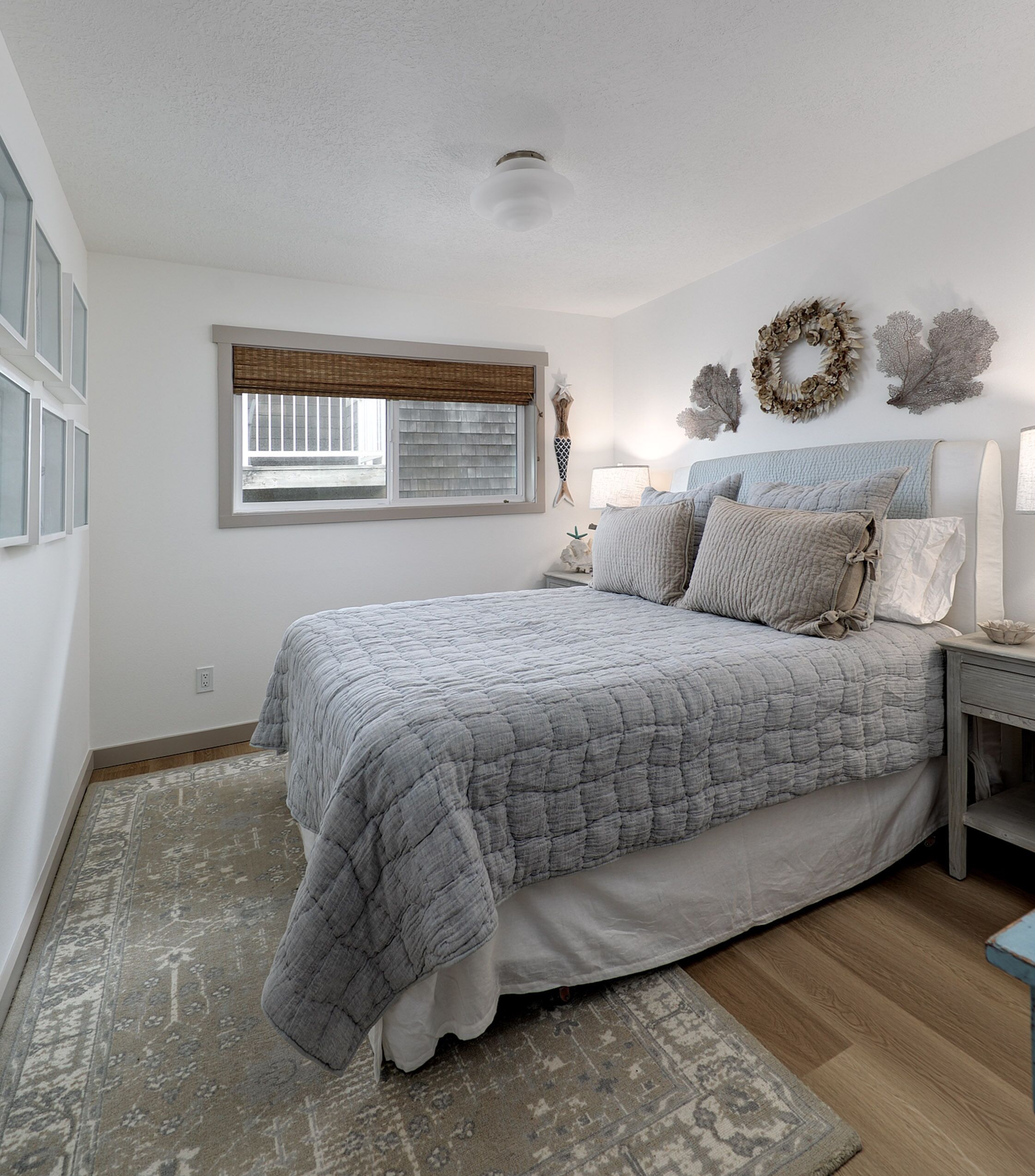 A bedroom with a large bed, a nightstand, a lamp, a window with blinds, and wall decorations.