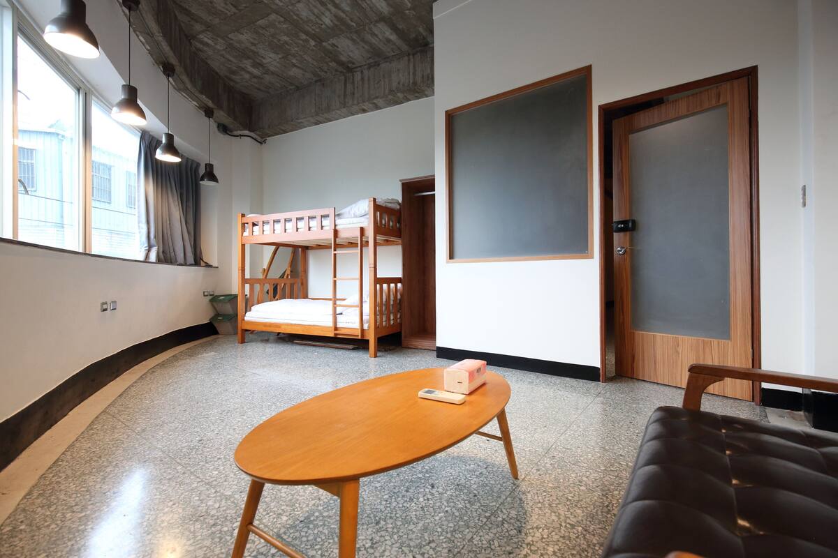 A room with bunk beds, a wooden table, a sofa, and a large window with curtains.