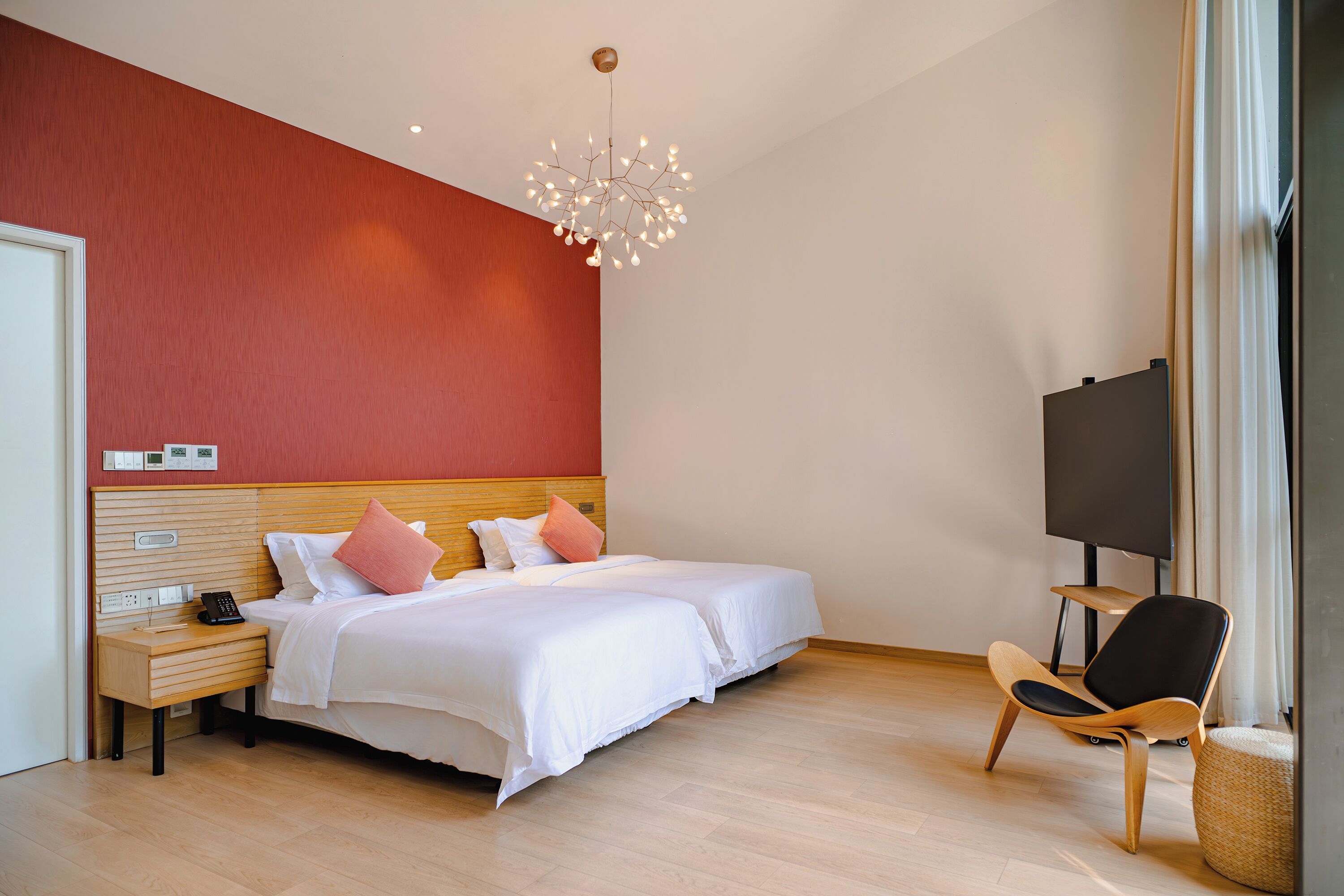 A hotel room with two beds, a wooden nightstand, a modern chair, and a flat-screen TV.