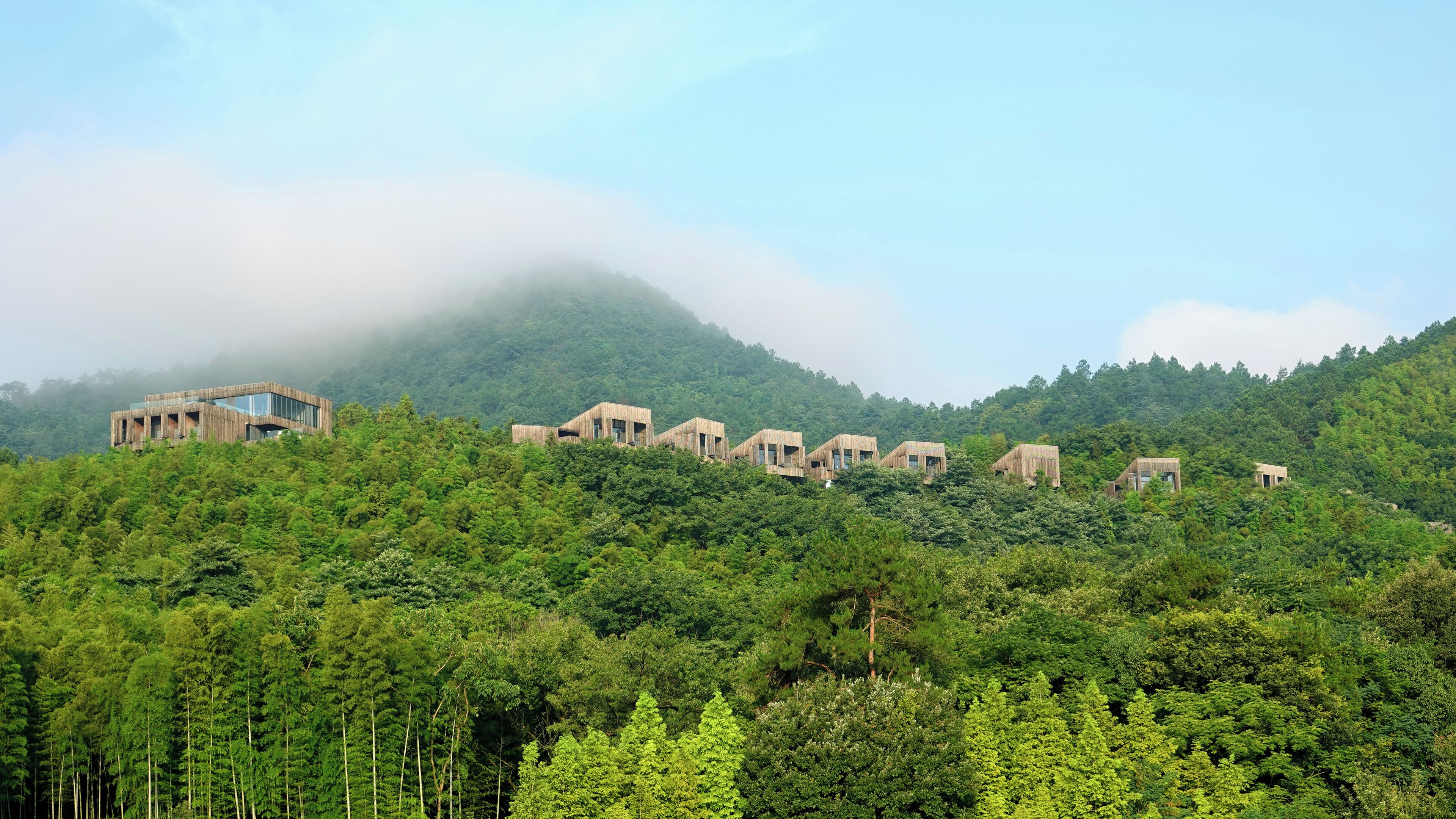 A series of wooden cabins on a hillside with dense forest.