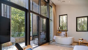 Une chambre d’hôtel moderne dotée d’une grande porte-fenêtre coulissante donnant sur un balcon, d’une baignoire blanche et d’un téléviseur à écran plat.