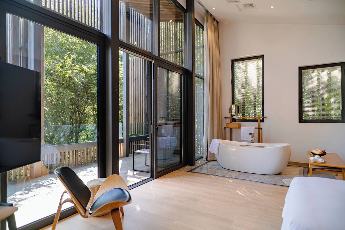Ein modernes Hotelzimmer mit einer großen Schiebeglasdoor, die auf einen Balkon führt, einer weißen Badewanne und einem Flachbildfernseher.