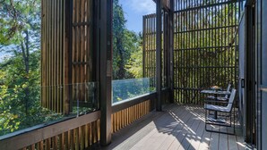 Une terrasse en bois dotée d’une rambarde en verre, offrant une vue sur une zone boisée.