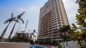 Un grand hôtel doté de nombreux balcons, entouré de palmiers et comprenant un espace piscine.