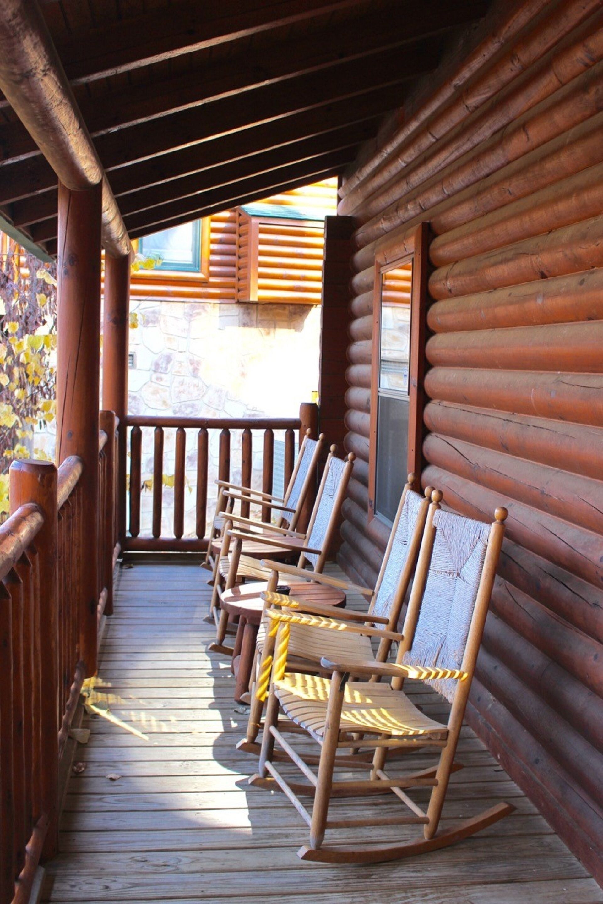 A wooden porch with rocking chairs and a stone wall in the background.