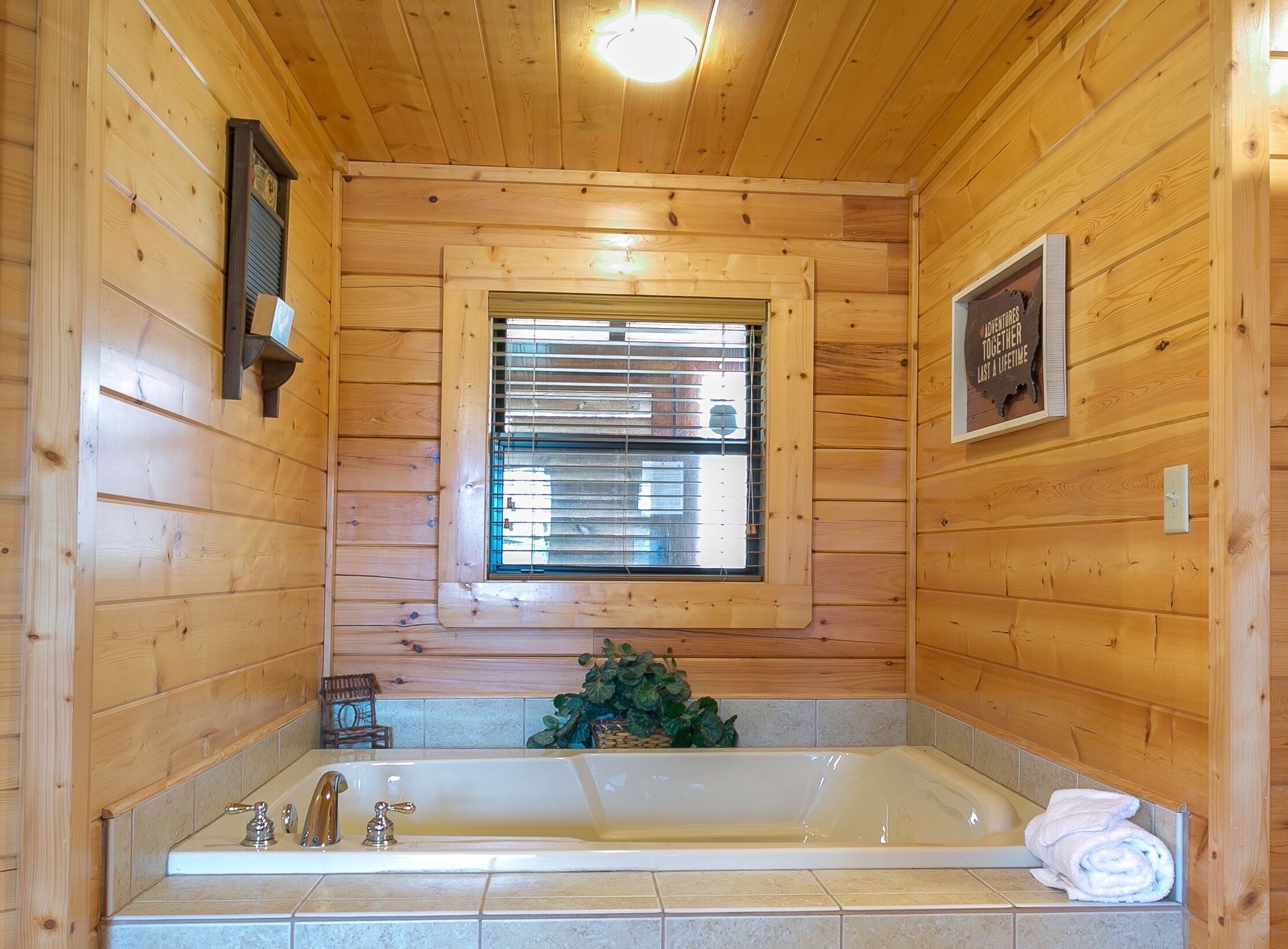 Une salle de bain rustique, aménagée dans une cabane en bois, avec une baignoire, une fenêtre et un tableau encadré au mur.
