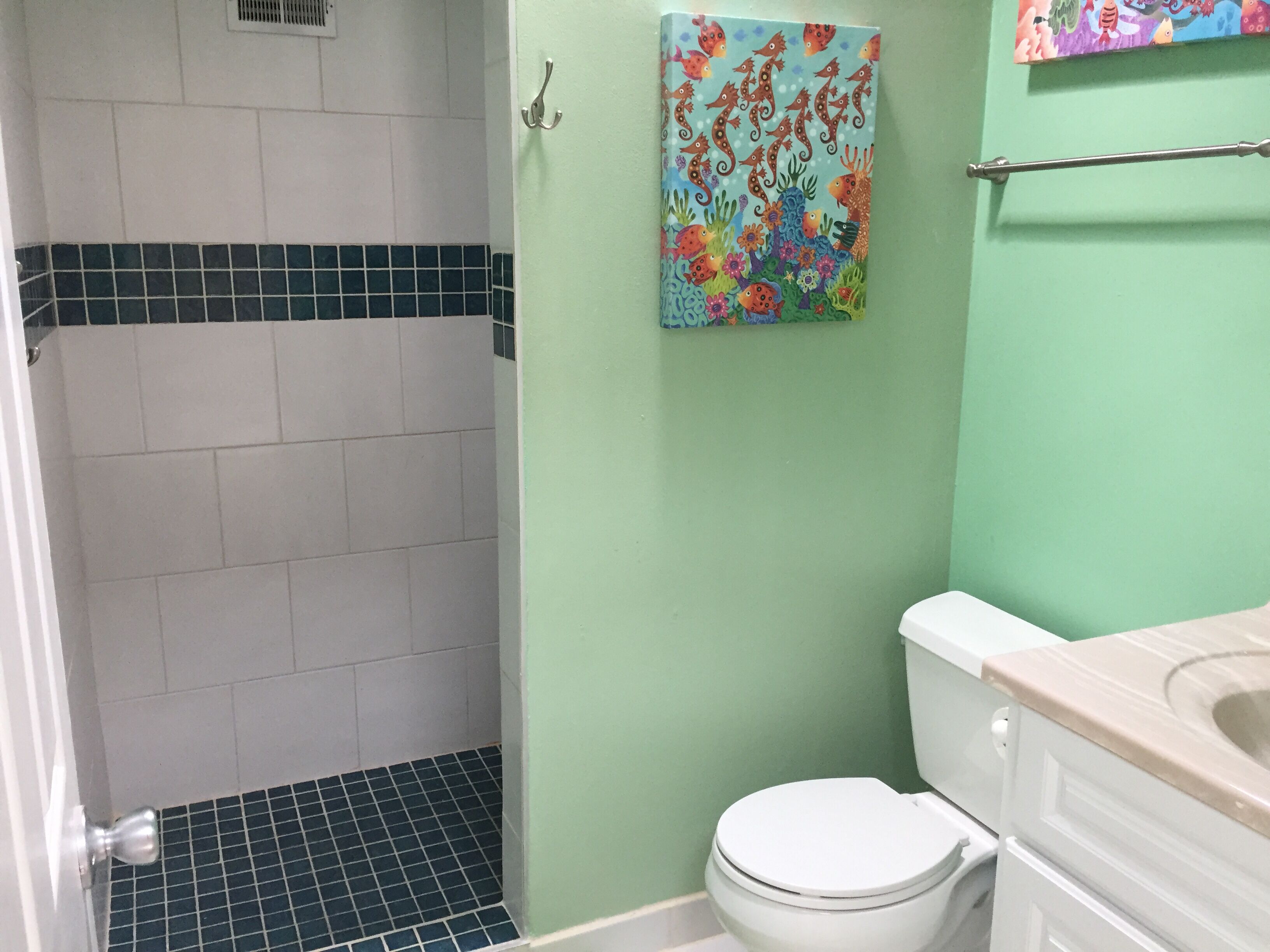 Une salle de bain avec des toilettes blanches, un mur vert et un espace douche carrelé de blanc et de bleu.