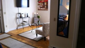 A living room with a flat-screen TV mounted on the wall, a patterned armchair, a small round table with a vase and candles, and a wooden floor. - Marine On St Croix Retreat, Unit 1 (Marine On Saint Croi)