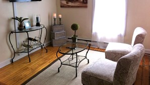 A living room with a TV mounted on the wall, a glass coffee table, a patterned armchair, a small table with candles, and a painting above the coffee table. - Marine On St Croix Retreat, Unit 1 (Marine On Saint Croi)