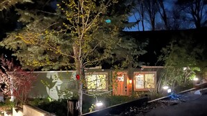 Vista nocturna de una casa con puerta de garaje visible, un árbol en primer plano e iluminación de una farola.