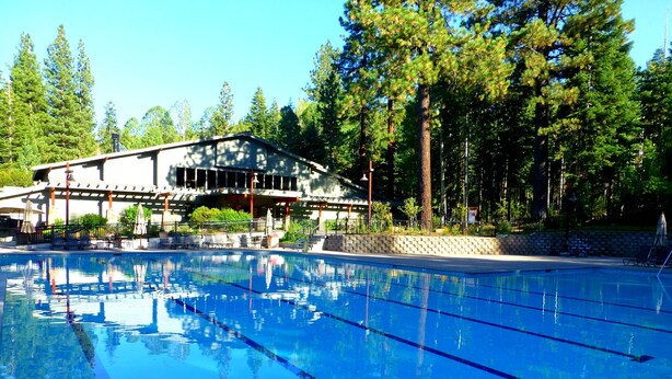 A swimming pool with clear blue water, surrounded by a wooden deck and lounge chairs.