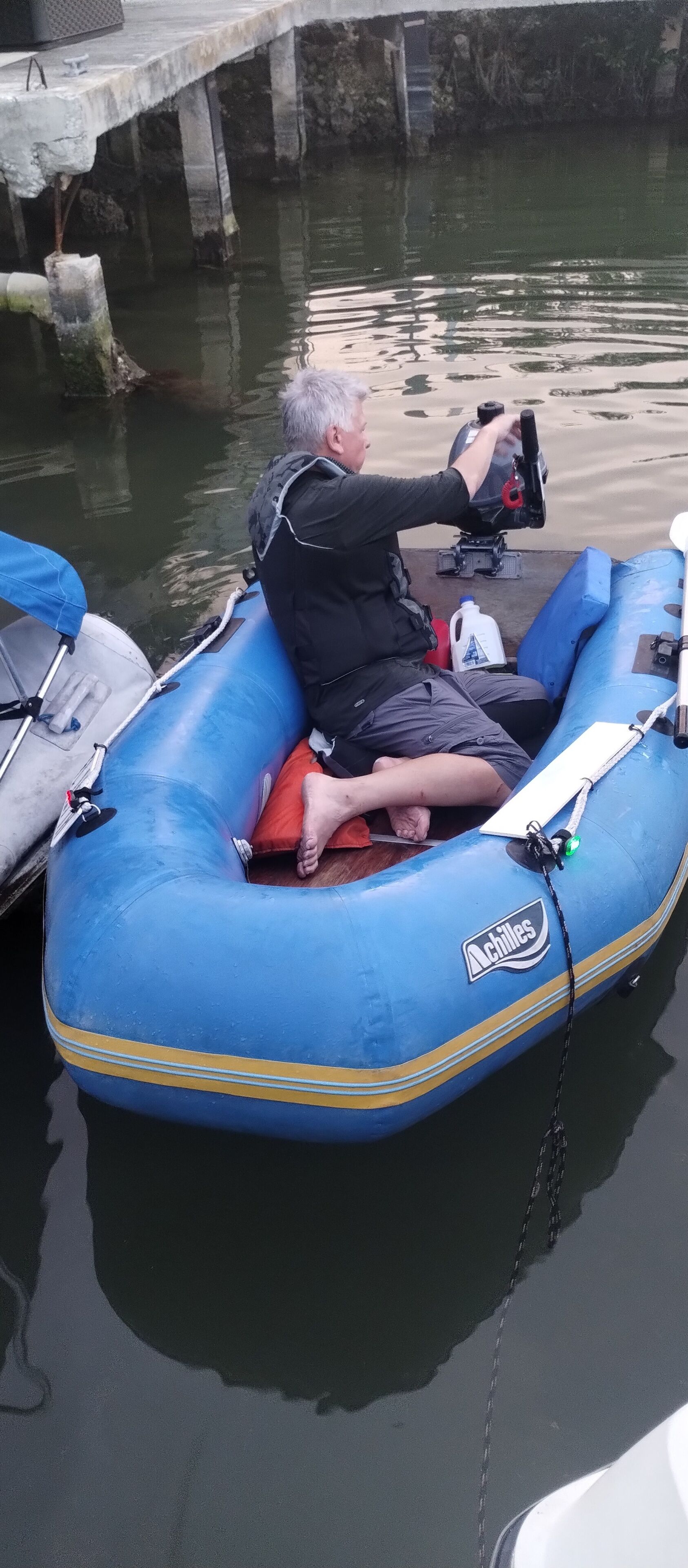 Un hombre sentado en un bote inflable azul en un muelle.