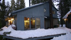 Una cabaña moderna con terraza, rodeada de nieve y árboles.
