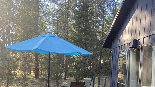 An outdoor deck with wicker furniture, a blue umbrella, and a view of the surrounding forest.