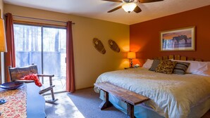 A bedroom with a bed, a desk, a chair, a ceiling fan, and a window with curtains.