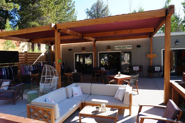 An outdoor seating area with a wooden pergola, cushioned sofas, and wooden tables.