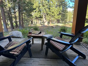 A covered outdoor seating area with two lounge chairs and a table, surrounded by trees and a view of a forested area.