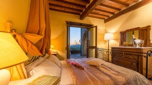 Ein Schlafzimmer mit Bett, Nachttisch mit Lampe, einem Fenster mit Vorhängen und Blick ins Freie.