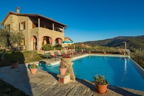 Una villa de piedra con piscina, mobiliario exterior y vistas a las colinas.