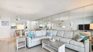 Ein modernes Wohnzimmer mit einem Ecksofa, einem Couchtisch und einem großen Spiegel, der den Raum reflektiert.