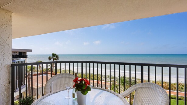 Ein Balkon mit Blick auf den Strand, ein Tisch mit einem Glas und Blumen sowie ein weißer Stuhl.