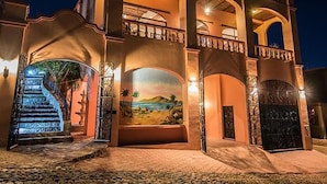 A large, multi-story building with a grand entrance, a staircase, and a mural depicting a coastal scene.