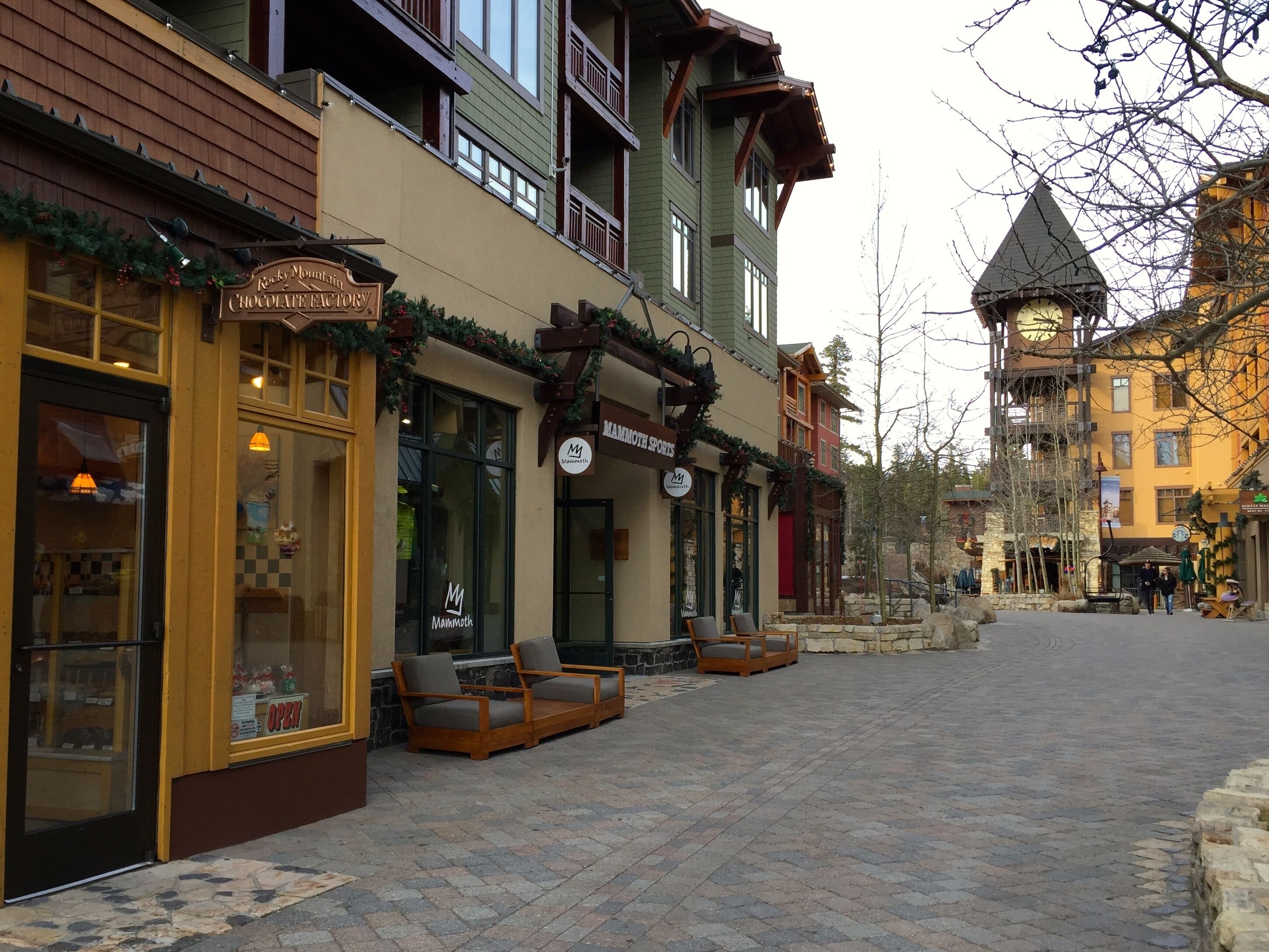 A cobblestone street with shops, including a chocolate factory and a mammoth sports store.