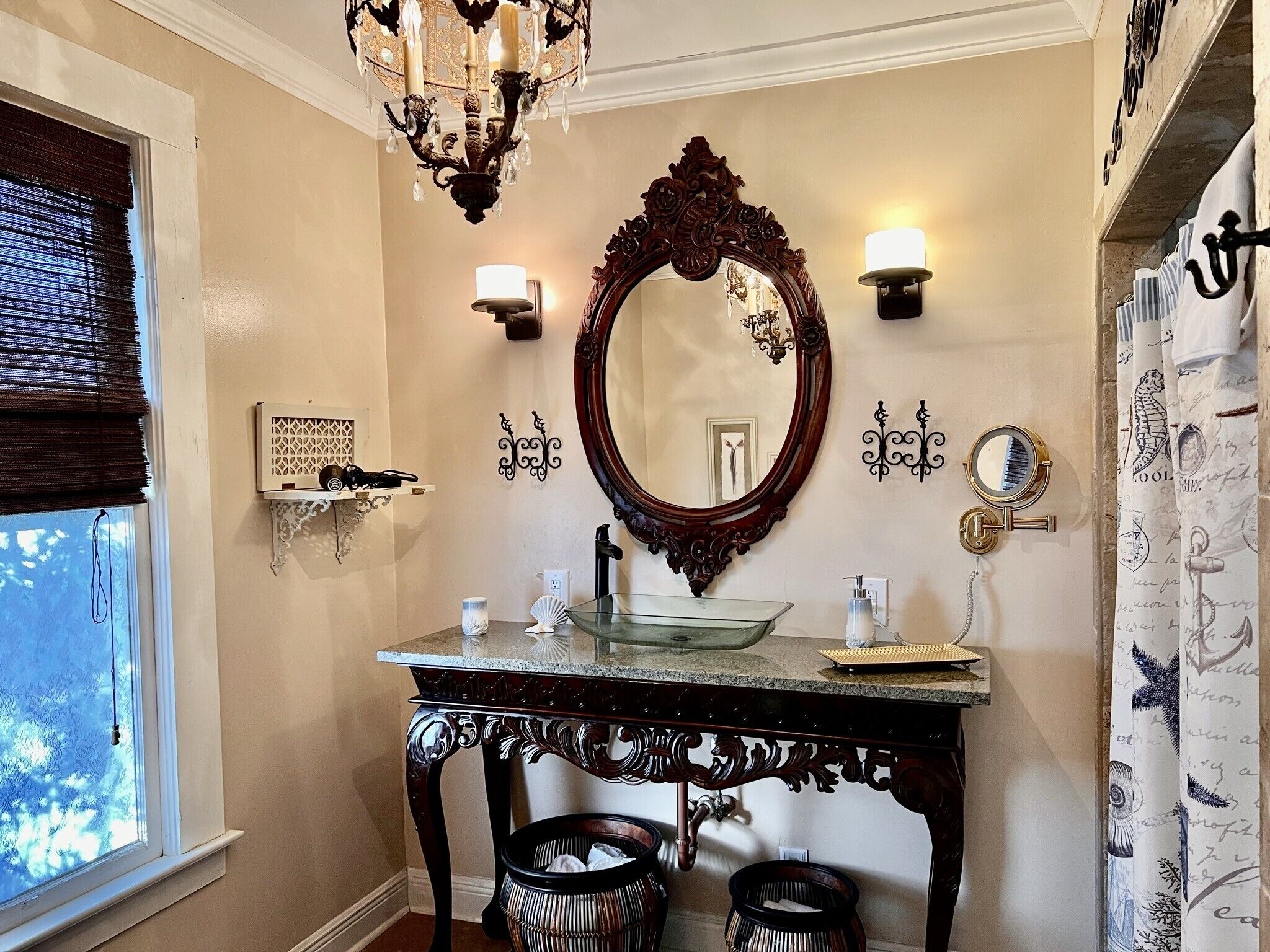 A bathroom with a large ornate mirror, a chandelier, and a vanity with a glass bowl.