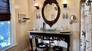 A bathroom with a large ornate mirror, a chandelier, and a vanity with a glass bowl. - Stylish Coastal Escape | 3BR Shabby Chic + Optional Cottage, Walk to Beach & Fun (Gulfport)