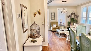 A cozy living room with a white console table, a green armchair, and a wooden floor. - Stylish Coastal Escape | 3BR Shabby Chic + Optional Cottage, Walk to Beach & Fun (Gulfport)