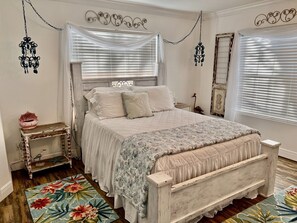 Ein Schlafzimmer mit einem hölzernen Bett, weißer Bettwäsche, Wanddekoration und einem floralen Teppich.
