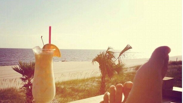 A beach view with a drink in a glass and a palm tree in the foreground. - Stylish Coastal Escape | 3BR Shabby Chic + Optional Cottage, Walk to Beach & Fun (Gulfport)
