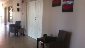 Un couloir avec une porte fermée, une petite table sur laquelle se trouve une plante, et deux chaises.