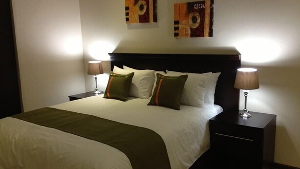 Une chambre d’hôtel avec un grand lit, deux tables de chevet avec des lampes et deux œuvres d’art accrochées au mur au-dessus du lit.