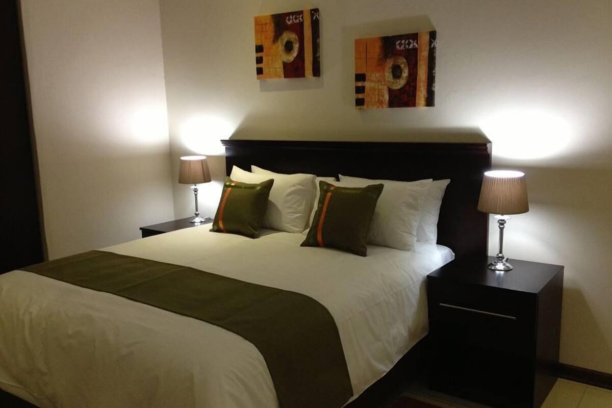 Una habitación de hotel con una cama grande, dos mesitas de noche con lámparas y dos cuadros en la pared sobre la cama.
