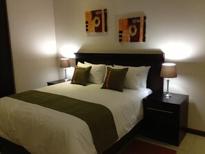 A hotel room with a large bed, two bedside tables with lamps, and two wall art pieces above the bed. - Emerald Hotel (Gaborone)